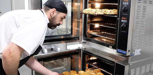 A chef leans towards an oven as he takes out a tray of scones.