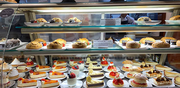 A open display case of desserts consisting of chocolate cakes, cream-filled scones, and pastries.